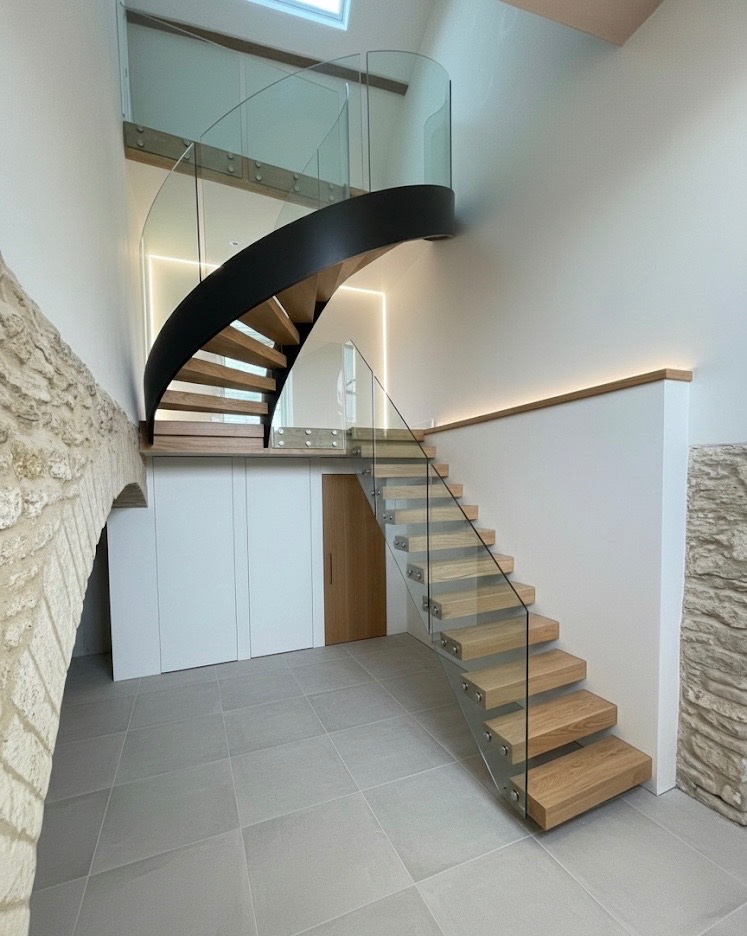 Wooden open-riser staircase with glass balustrades leading to a curved upper flight with a black outer stringer.