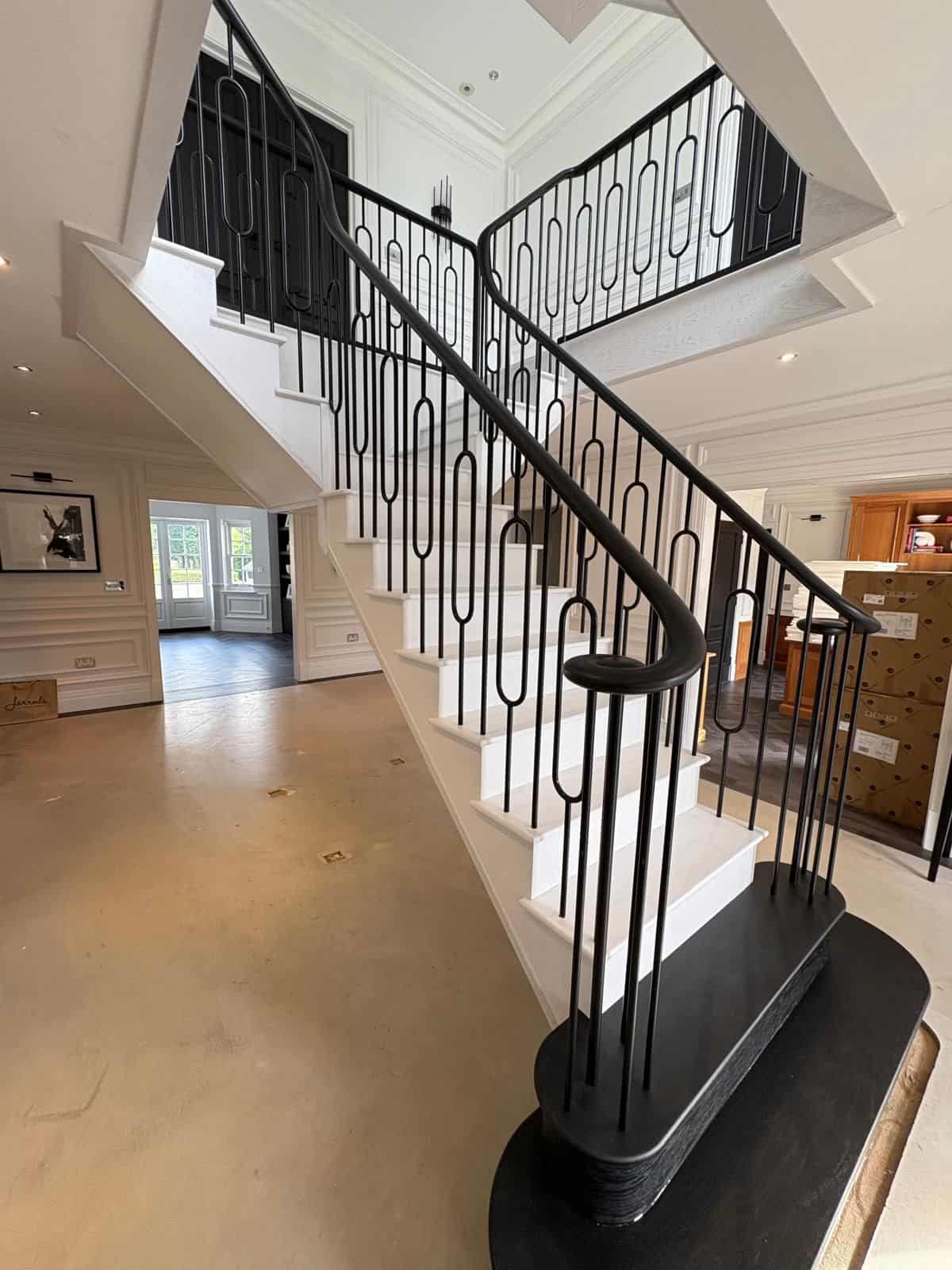 White staircase with black metal balustrades featuring elongated oval details and a curved black handrail.