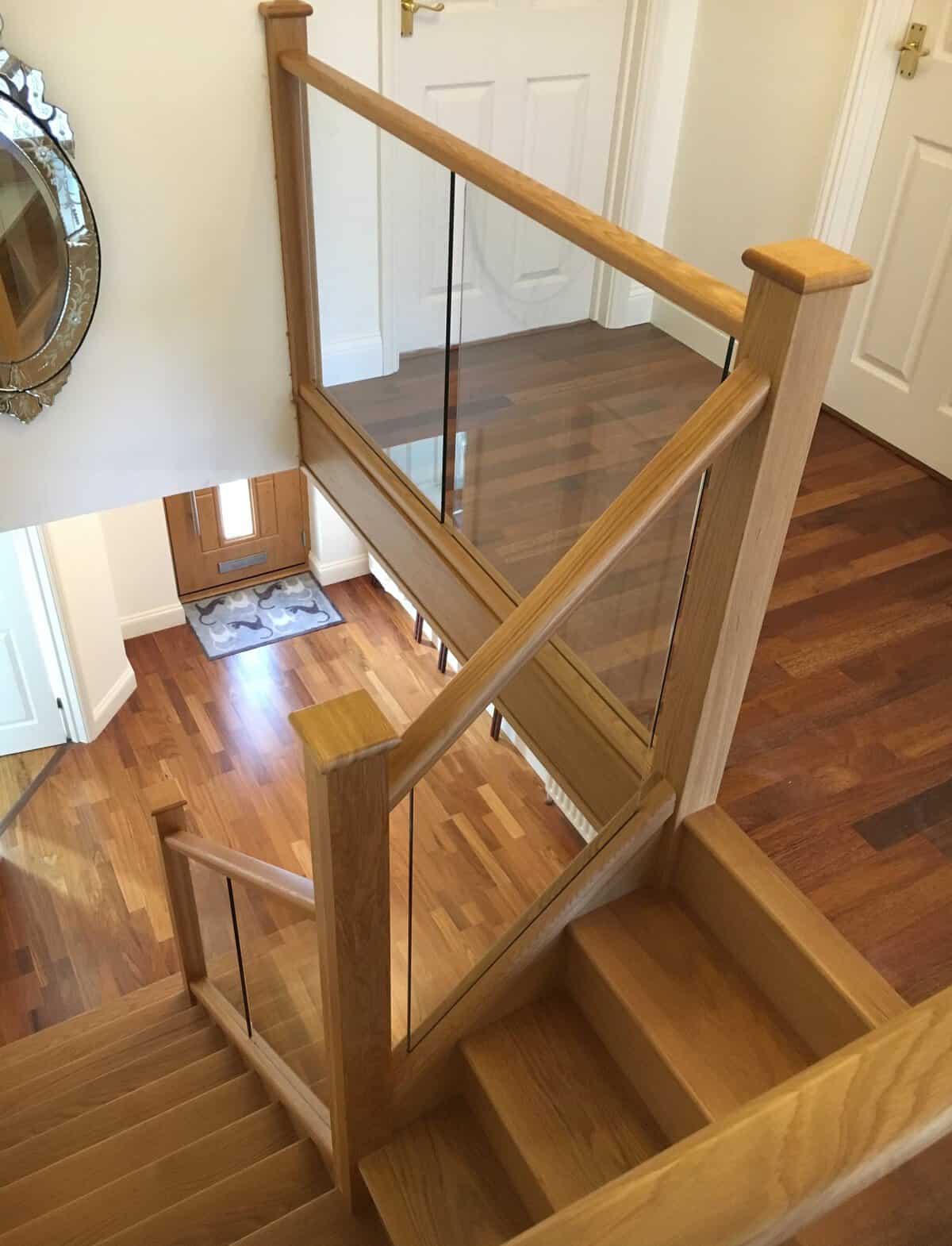 Oak staircase and landing with clear glass balustrades, square newel posts and matching wooden handrails, viewed from above.