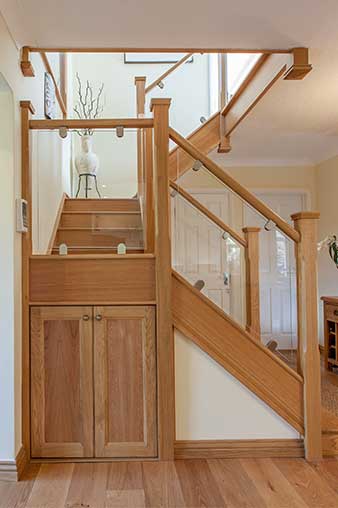 Oak turning staircase with clear glass panels secured by metal brackets and a fitted double-door wooden cupboard beneath the intermediate landing.