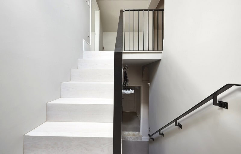 Modern staircase with light wood and black railing.