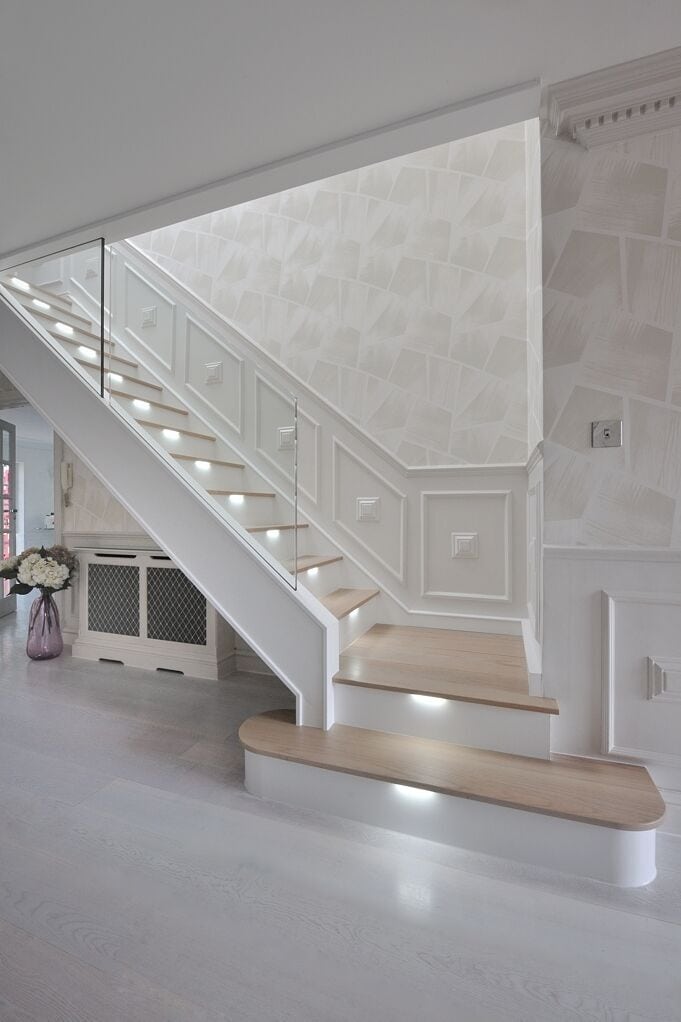 White staircase with wooden treads, recessed step lighting and broad rounded feature steps in a panelled hallway.