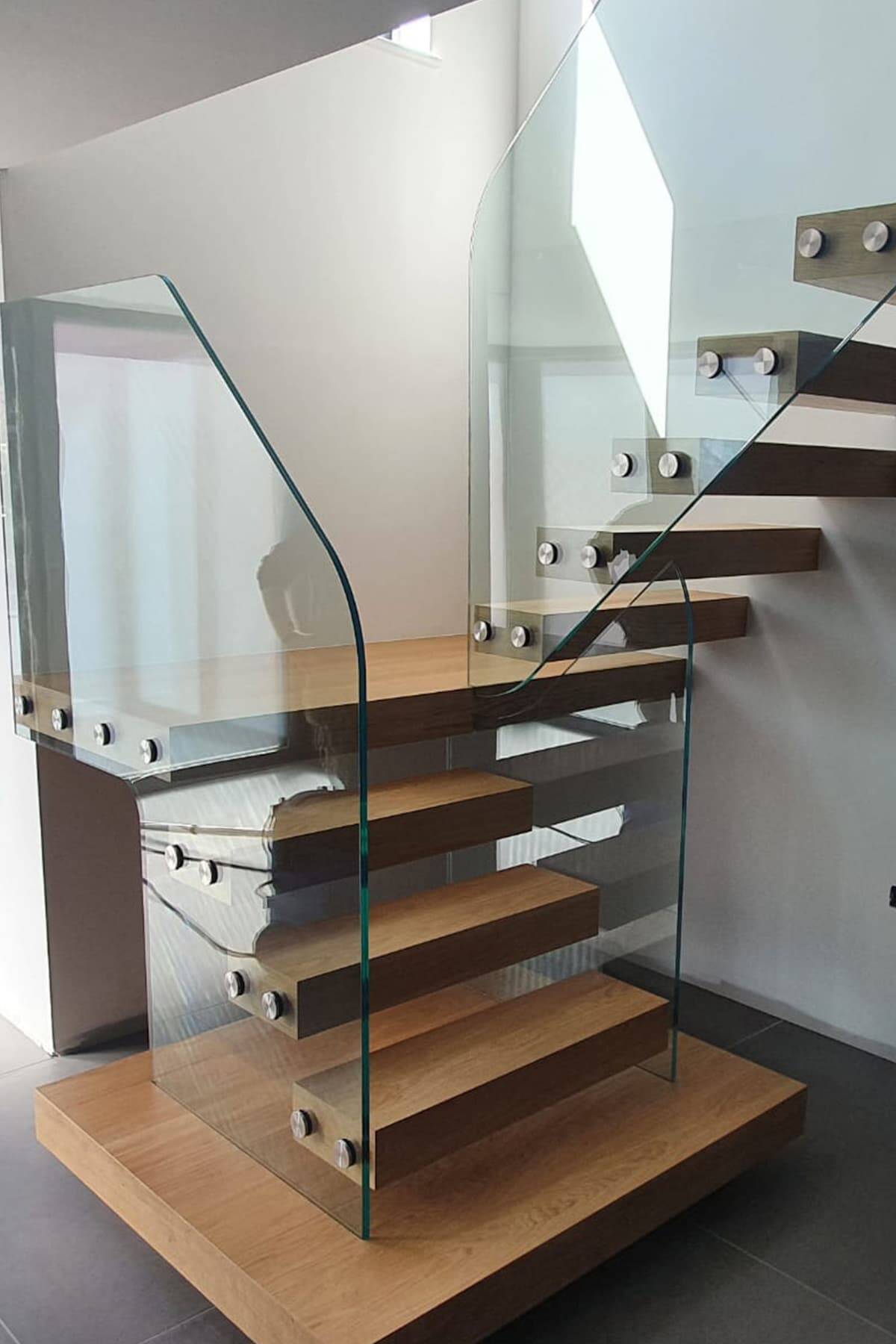Turning floating wooden staircase with open treads and shaped frameless glass panels secured by round metal fixings.