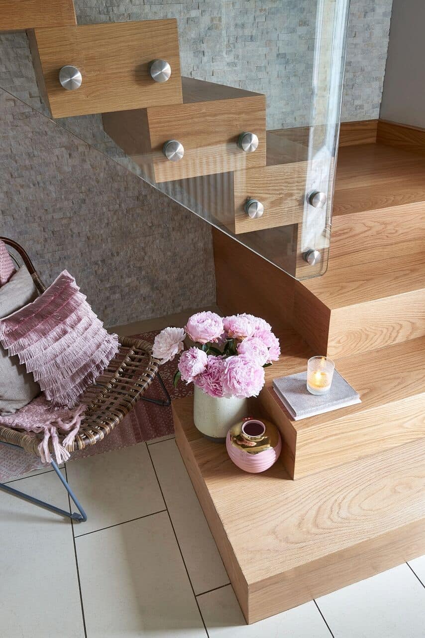 Close view of a turning oak staircase with thick timber treads and shaped glass balustrades secured with round metal fittings.