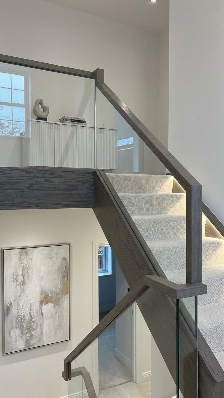 Grey-stained oak staircase with glass balustrades, square newel posts and light carpeted steps.