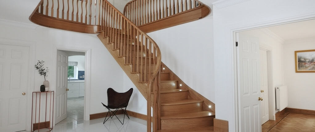 Sweeping oak staircase with shaped wooden spindles, recessed step lights and a matching curved gallery landing.
