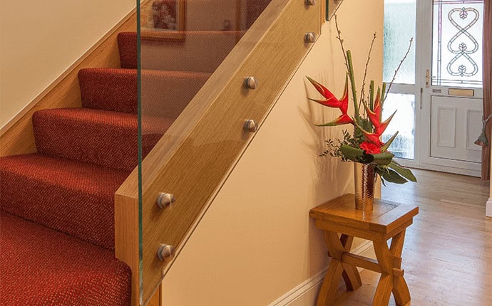Close-up of a red carpeted oak staircase with a frameless glass balustrade attached to the wooden stringer by round metal fixings.