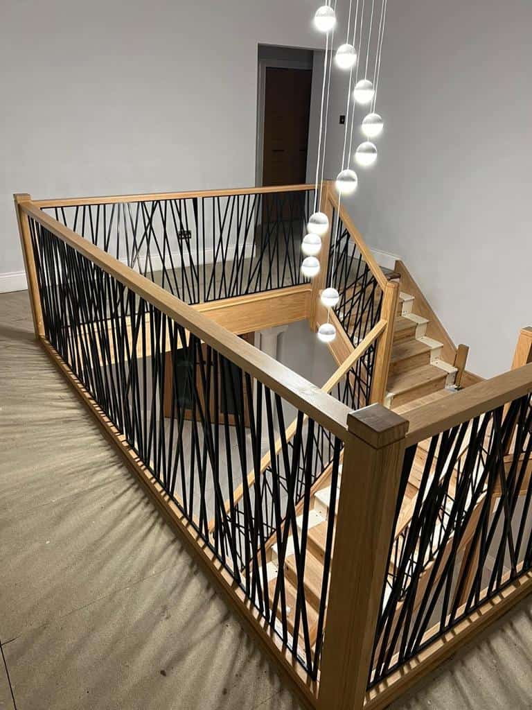 Renovated oak staircase and gallery landing with geometric black steel balustrades beneath a cascade of pendant lights.