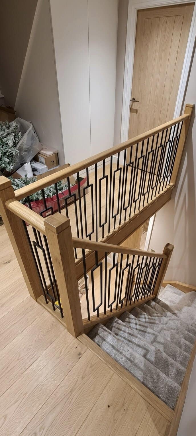 Renovated staircase and landing with square oak posts, oak handrails, geometric black steel balustrades and grey patterned carpet.