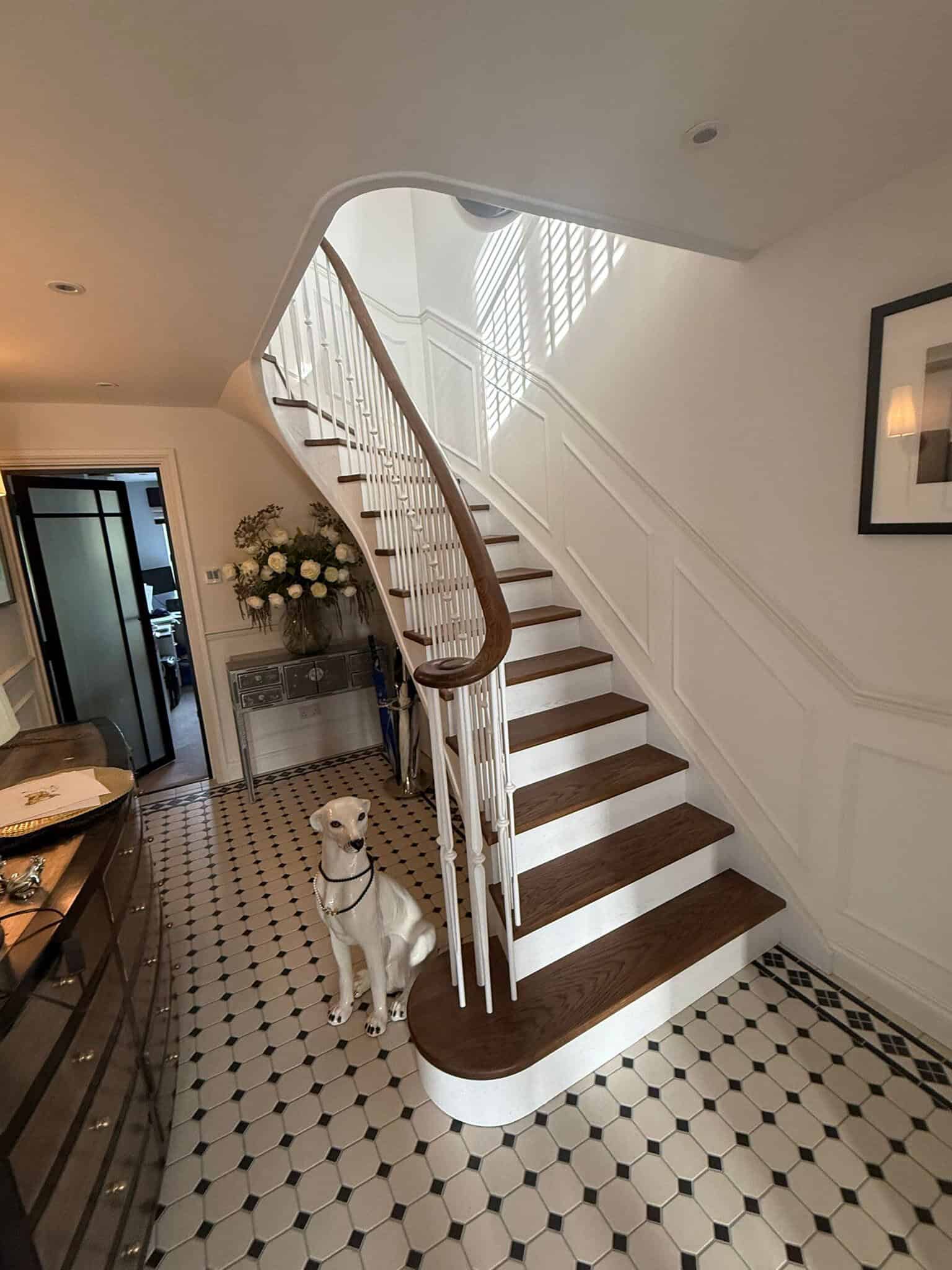 A flared, cut-string staircase in stained oak, featuring solid steel spindles with a white powder-coated finish and a stained oak wreath handrail