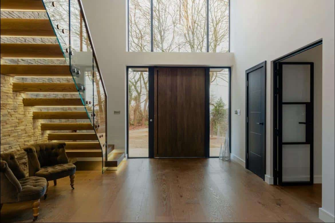 Floating wooden staircase with a glass balustrade beside a stone feature wall in a bright entrance hall.