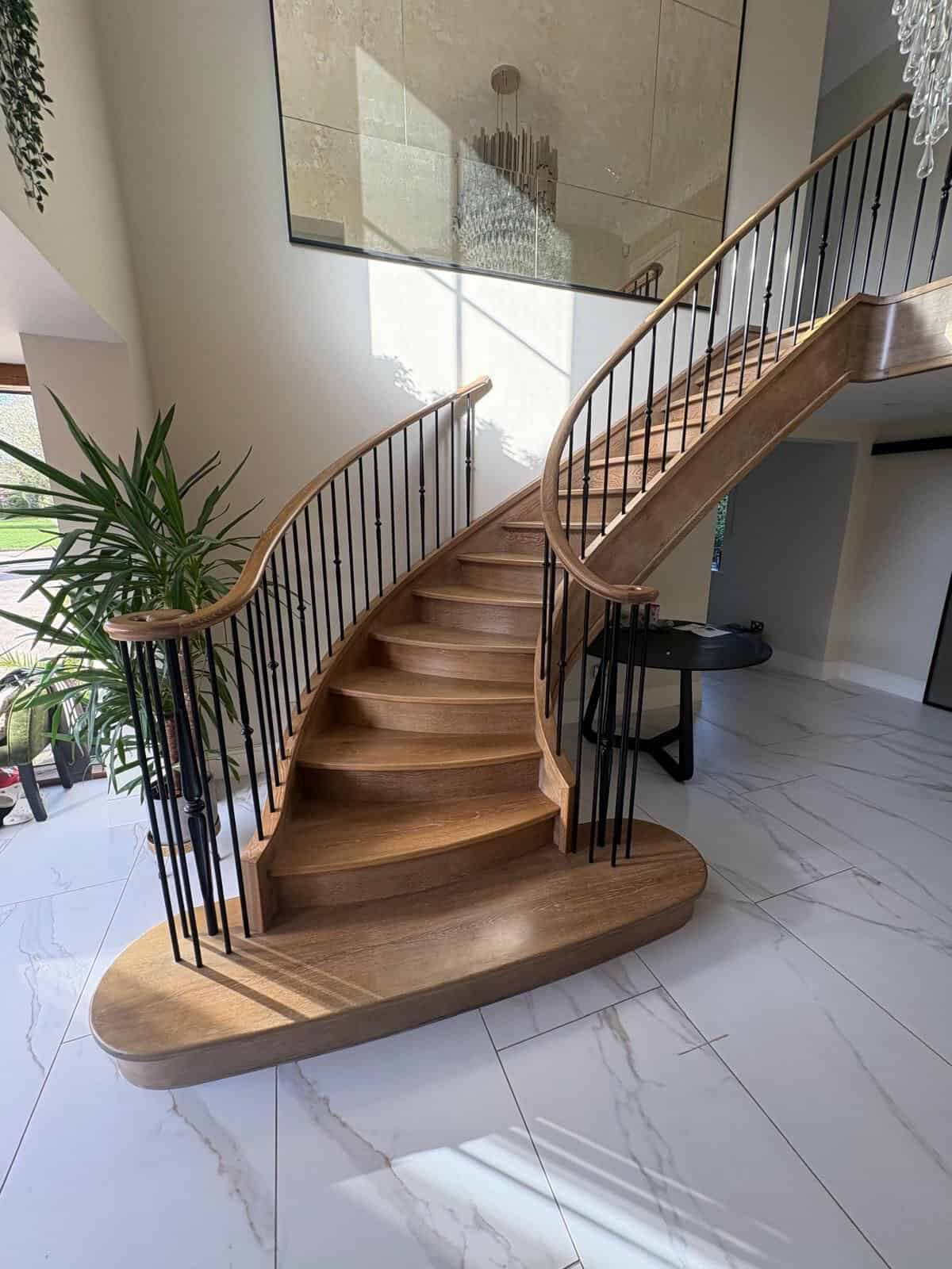 Curved oak helical staircase with bow-fronted treads, black steel spindles and wreathed wooden handrails above a broad rounded feature step.