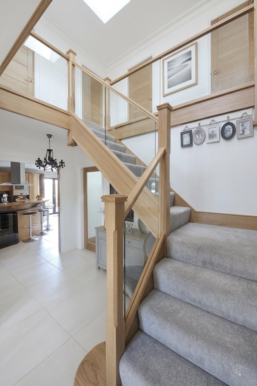 Oak staircase with glass balustrades, square newel posts and grey carpeted steps leading to a matching gallery landing.