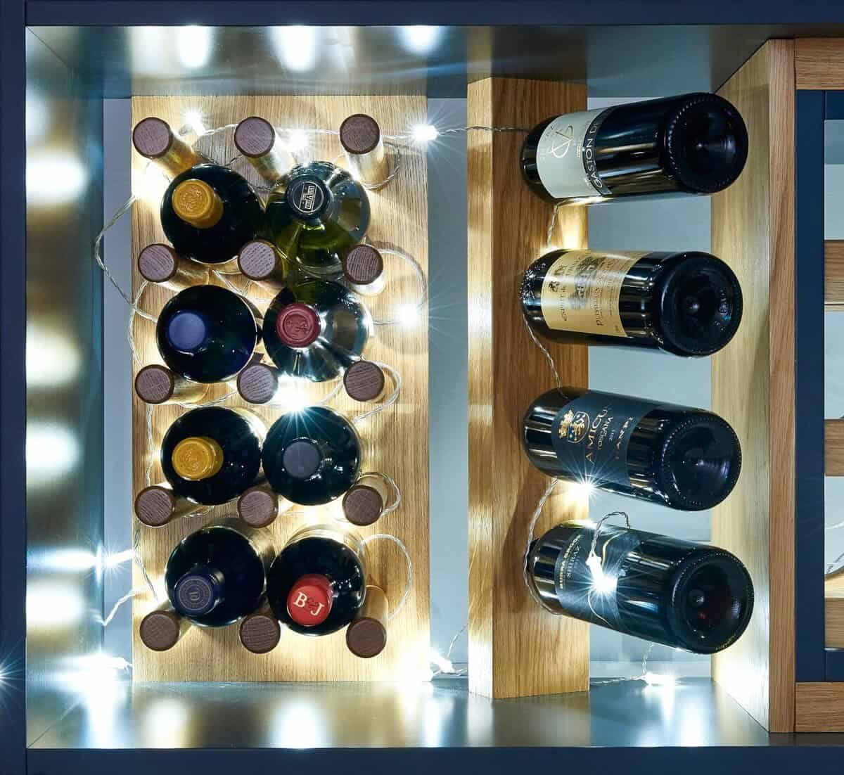 Illuminated wooden wine display with bottles resting on round pegs and horizontal supports against mirrored panels.