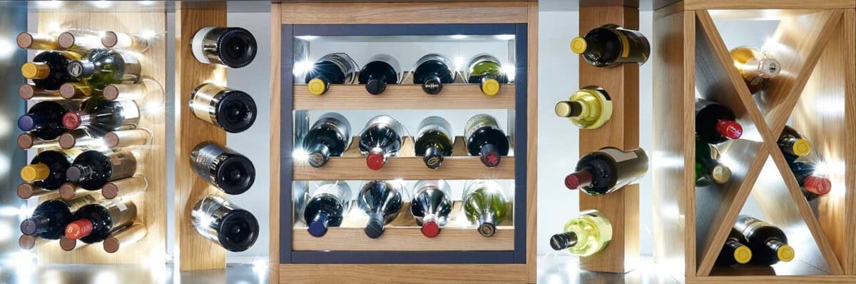 Illuminated wooden wine storage with individual bottle pegs, horizontal racks and a cross-shaped compartment filled with wine bottles.