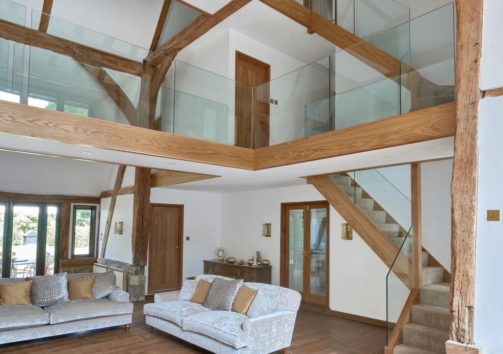Oak staircase and glass-fronted gallery landing beneath exposed timber roof beams in the Vallencey family double-height living room.
