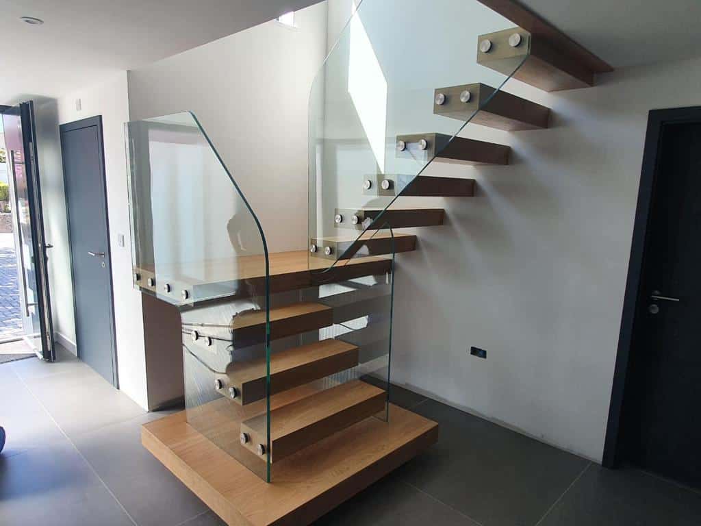 Floating wooden staircase with open treads and frameless glass balustrades fixed with round metal brackets.