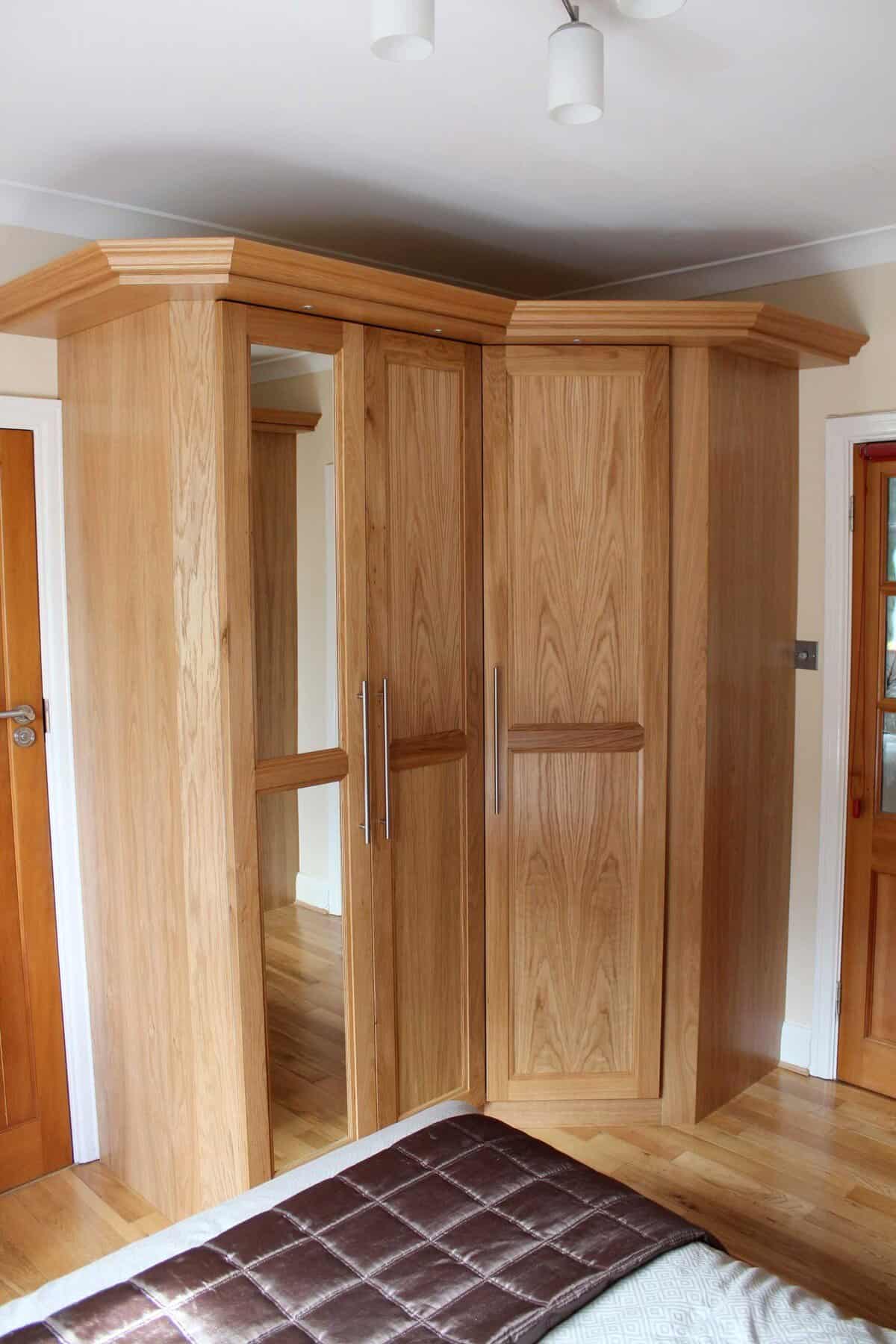 Fitted oak corner wardrobe with panelled doors, a full-length mirrored door, long metal handles and a moulded cornice.