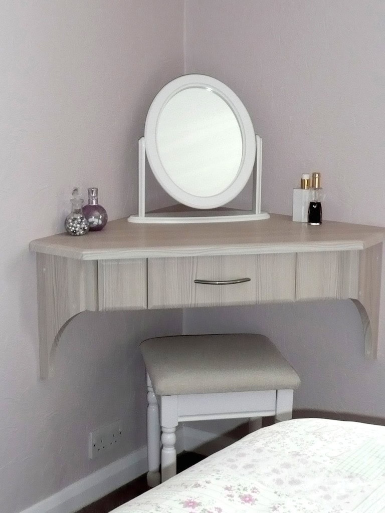 Bespoke pale wood corner dressing table with a single drawer, oval tabletop mirror and upholstered stool in a pink bedroom.