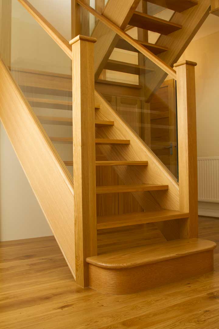 Oak open-riser staircase with integrated glass panels, square newel posts and a rounded wooden bottom step beneath a matching upper flight.