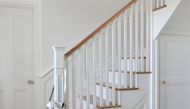 Close-up of a white painted staircase with slender square spindles, a shaped square newel post, oak tread edges and a natural wooden handrail.