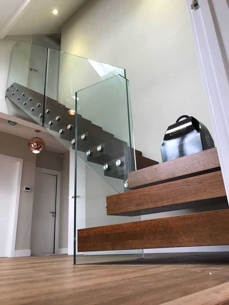 Open-riser staircase with dark wooden treads, a grey steel stringer and frameless glass panels secured by metal fixings.