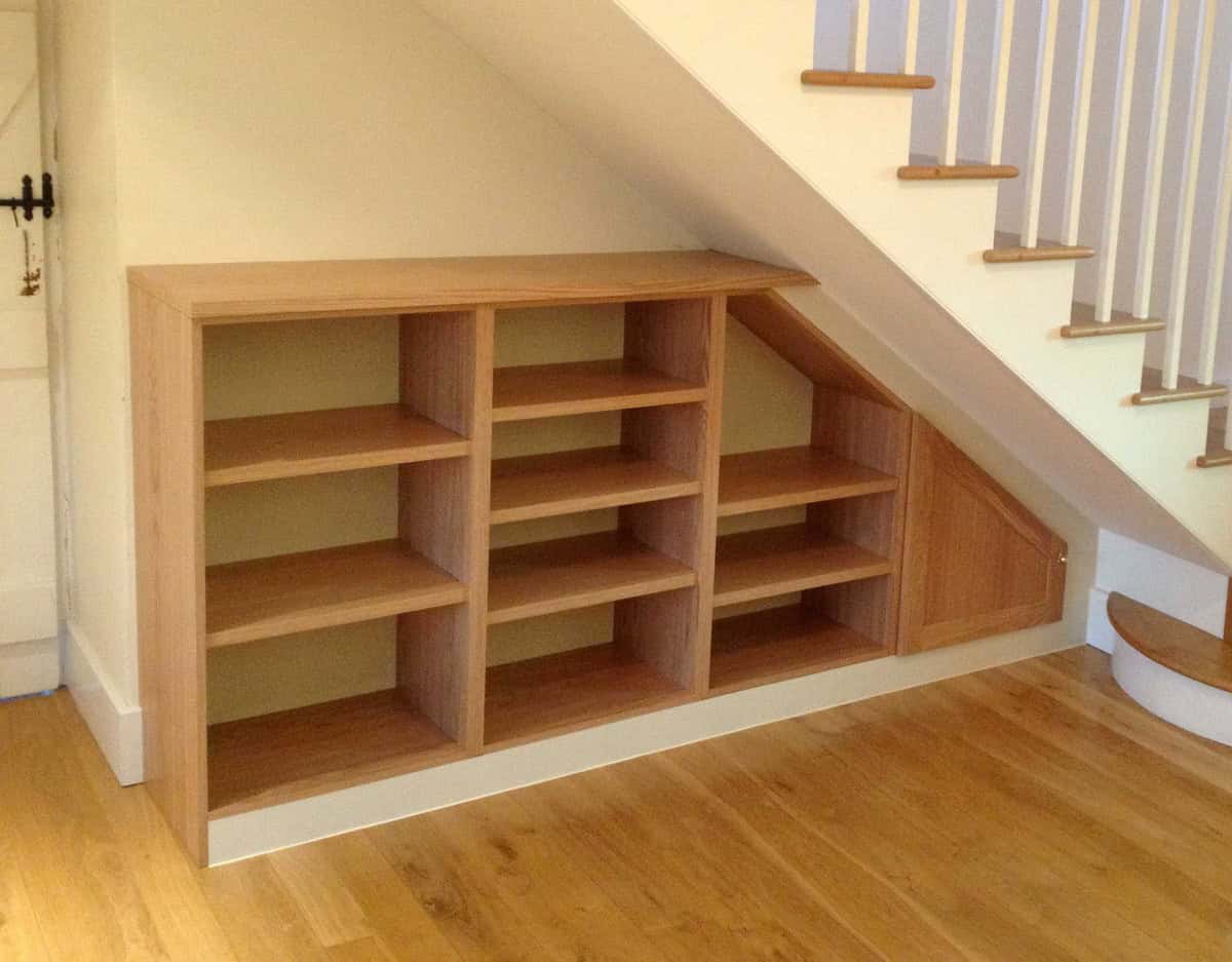 Bespoke oak open shelving and a triangular cupboard fitted beneath a white staircase with oak treads.