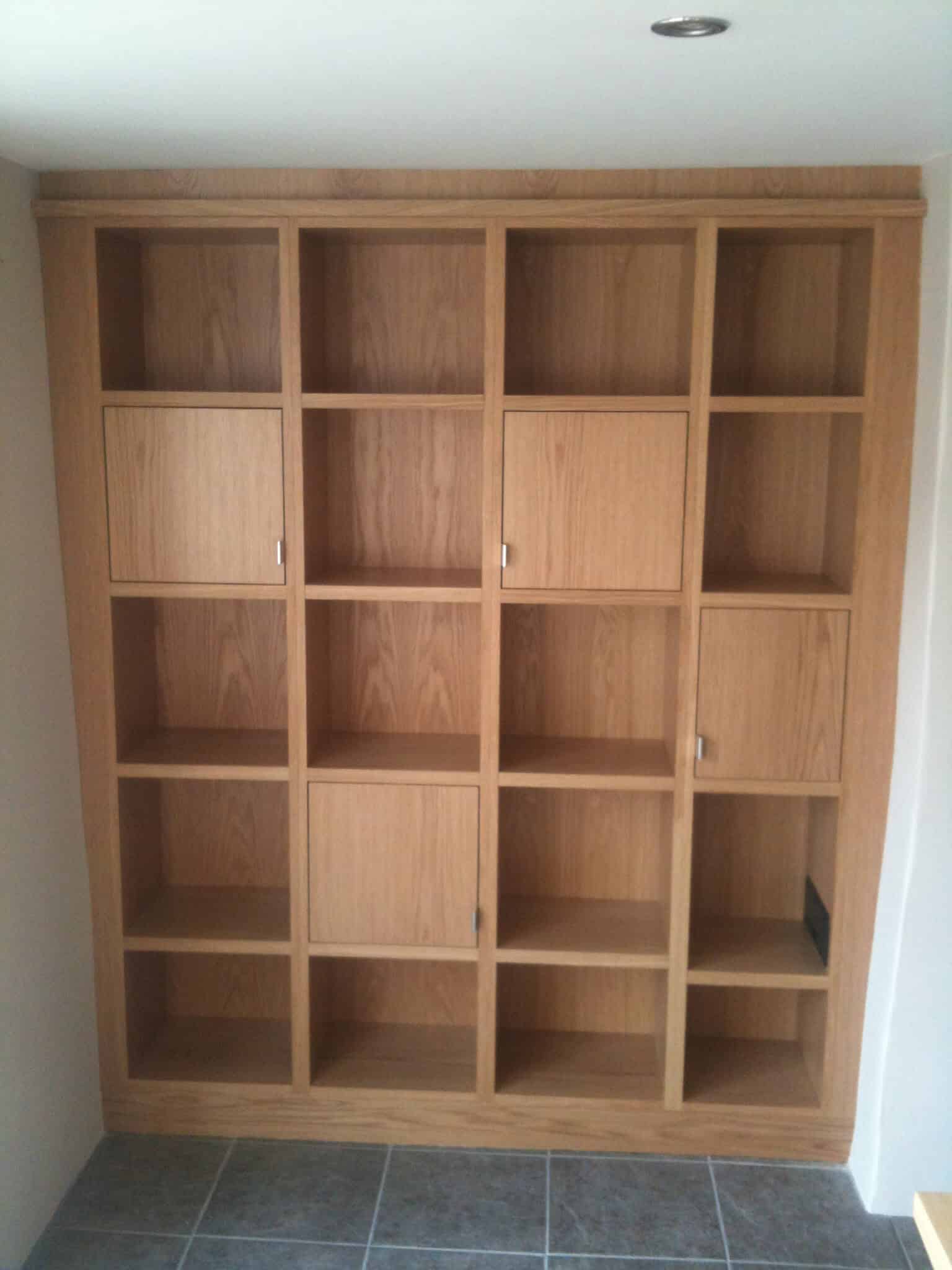 Full-height fitted oak shelving unit with a grid of open compartments and several inset cupboard doors in a recessed alcove.