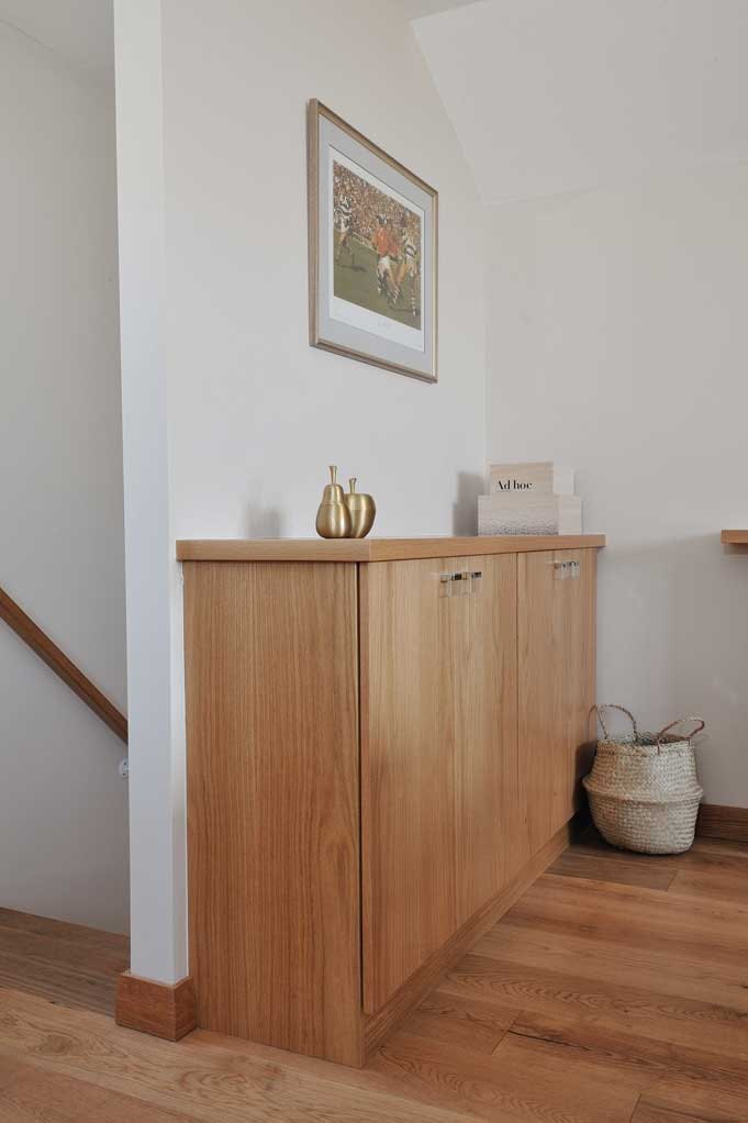 Fitted oak landing cabinet with flush wooden doors, small metal handles and a matching countertop beside the stairwell.