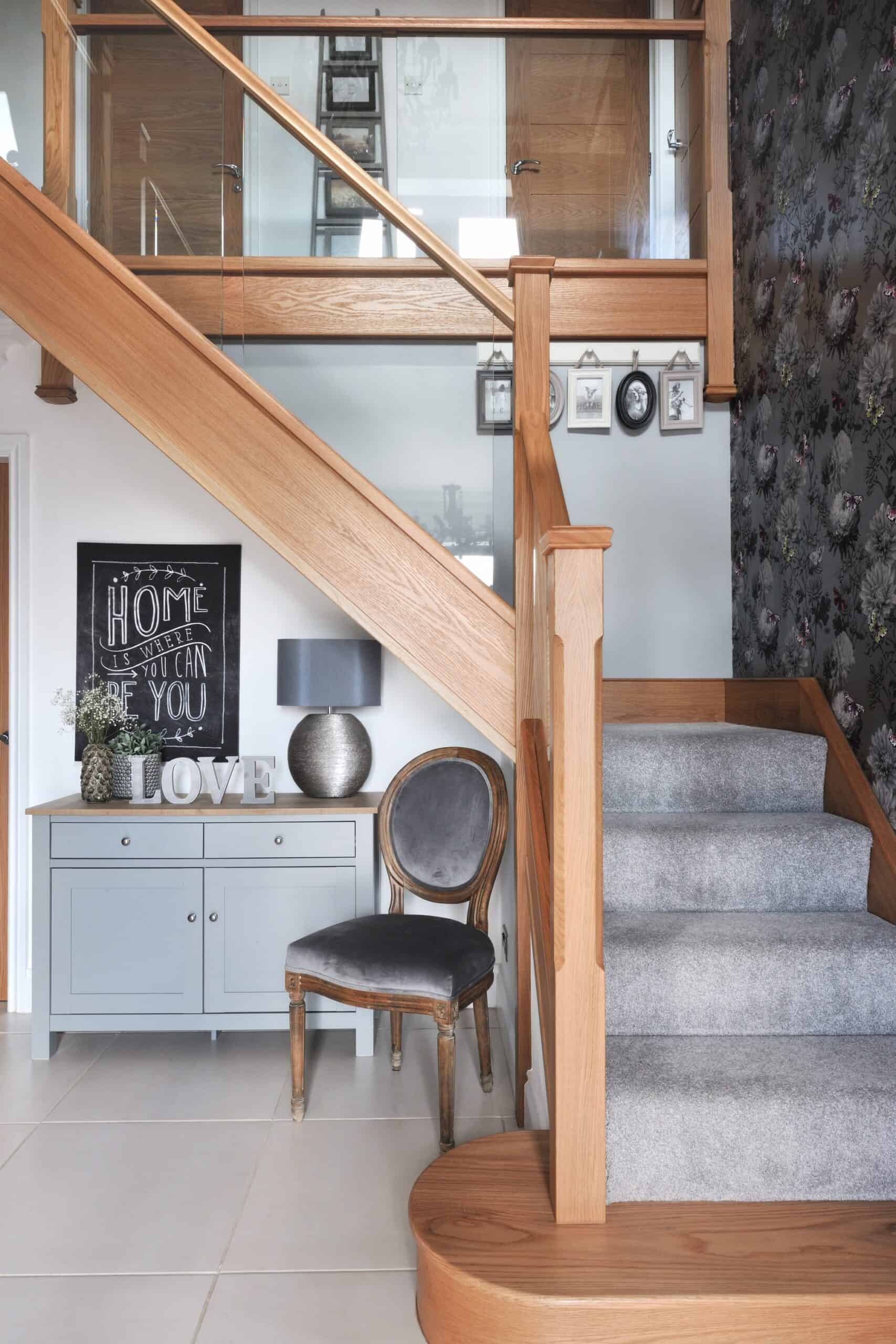 Oak staircase with glass balustrades, grey carpeted steps and a curved oak feature step in a tiled hallway