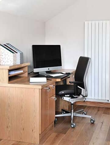 Compact fitted oak study desk with storage drawers, raised document shelves, a desktop computer and a black office chair.