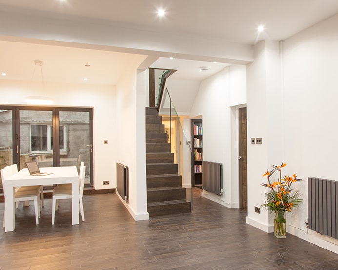 Dark wooden staircase with a glass balustrade set within a bright open-plan dining room with matching dark flooring.