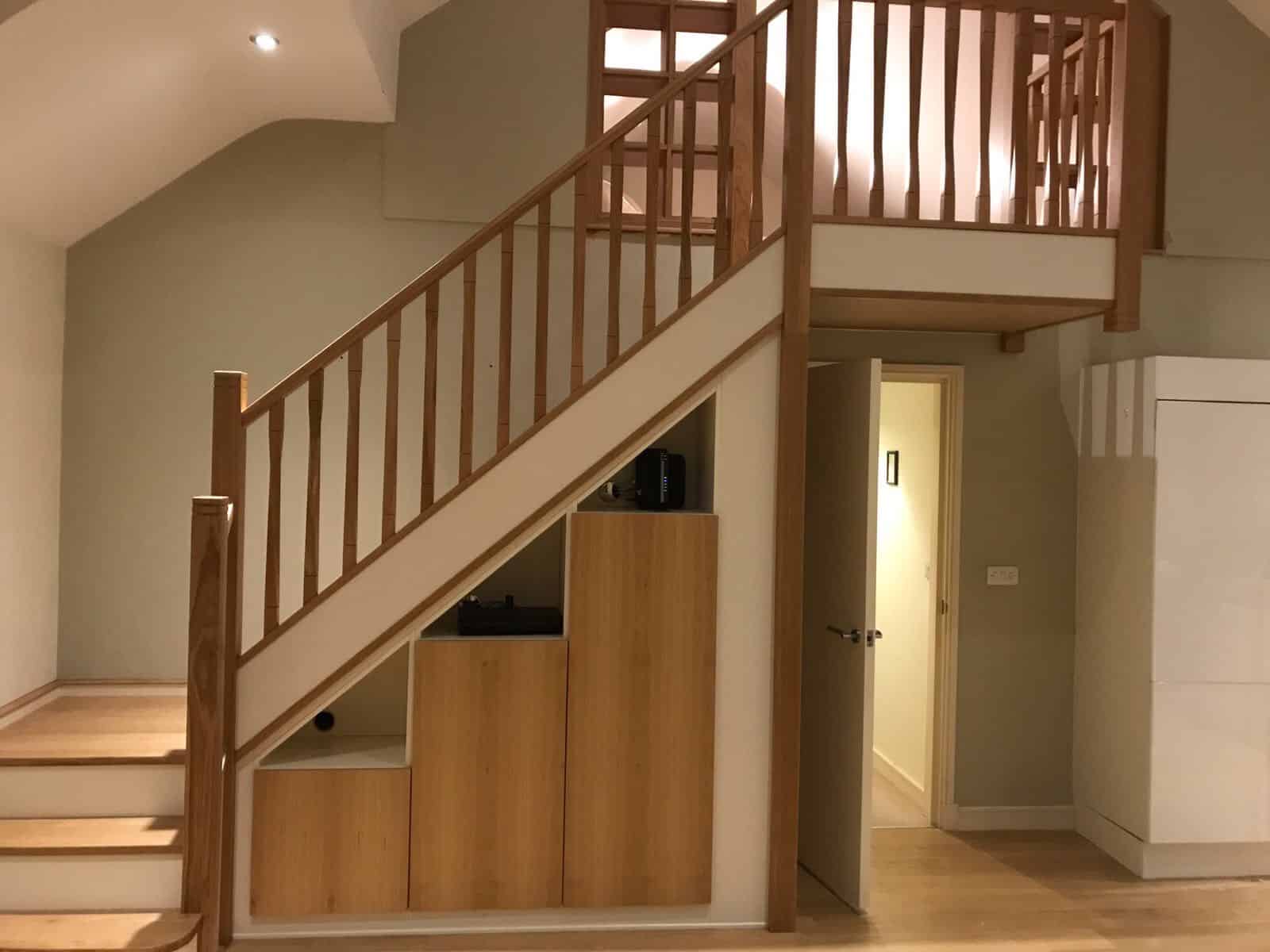 Oak staircase with square wooden spindles, white stringers and fitted stepped storage cupboards beneath the stairs.