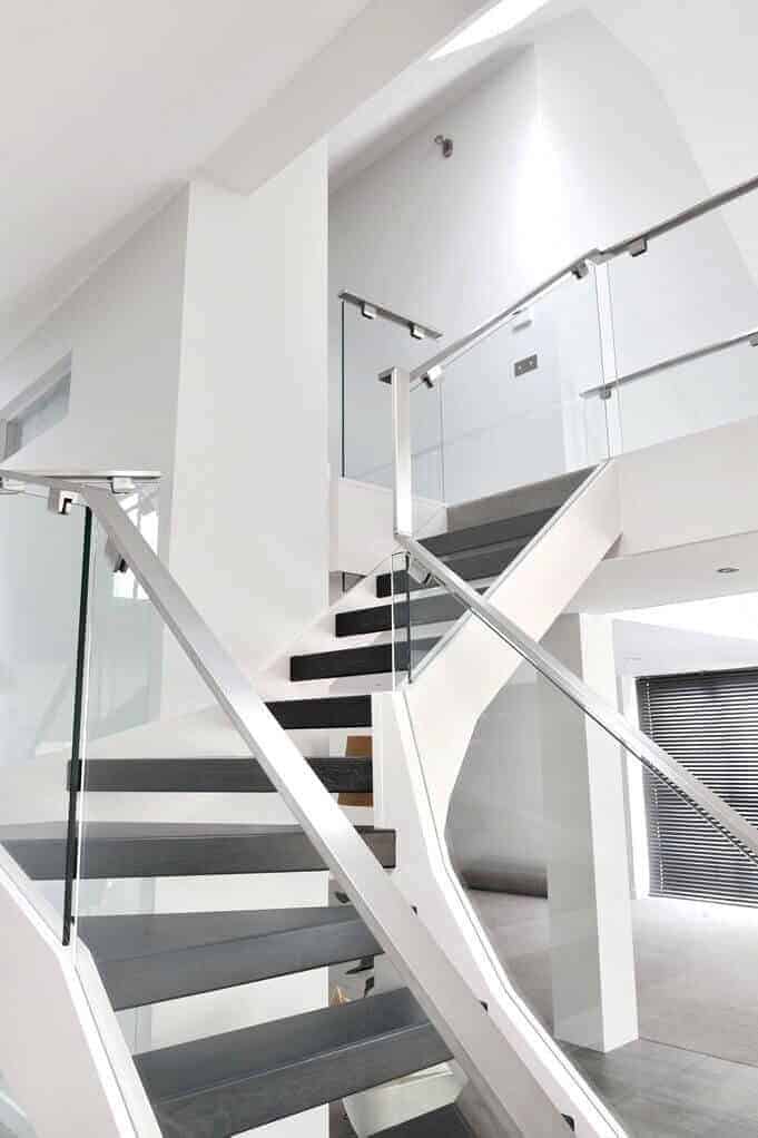 Turning open-riser staircase with dark treads, sculpted white stringers, glass balustrades and polished metal handrails leading to an upper gallery.