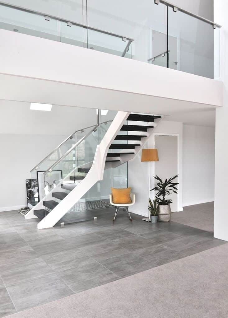 Contemporary staircase with curved white stringers, dark open treads and glass balustrades beneath a matching glass-fronted gallery landing.