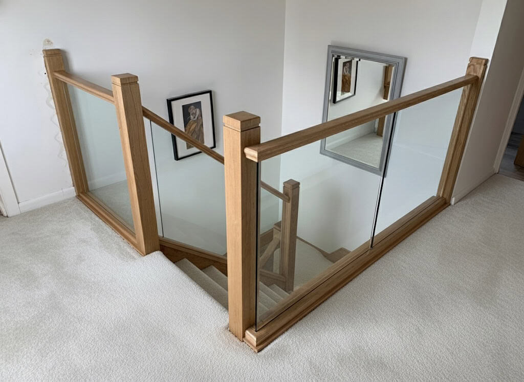 Clear glass balustrades enclosed by square oak posts and matching rails around a cream carpeted upstairs landing and stairwell.