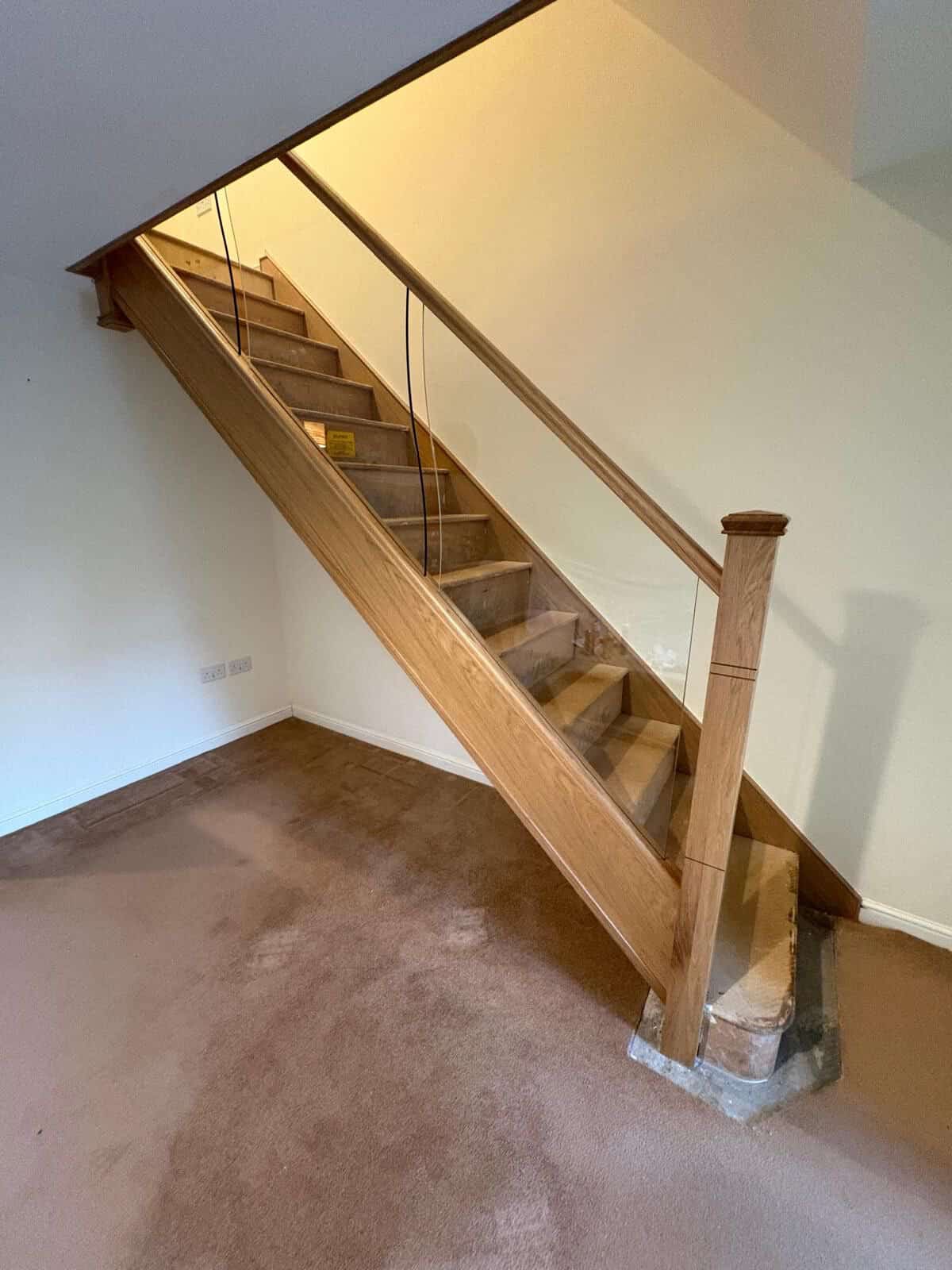 New oak staircase with integrated glass balustrades, a square newel post and closed wooden treads, with protective wrapping at the bottom step.