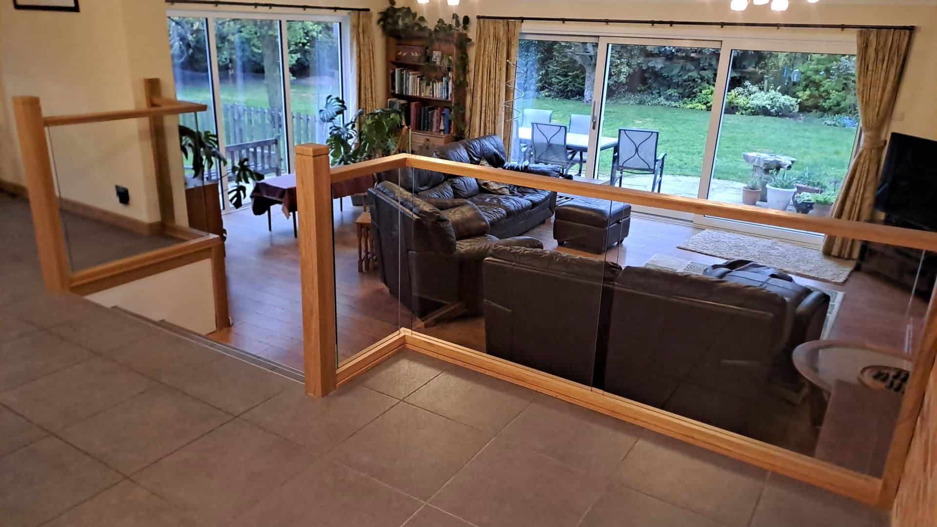 Oak-framed integrated glass balustrades separating a raised tiled area from a sunken living room overlooking the garden.