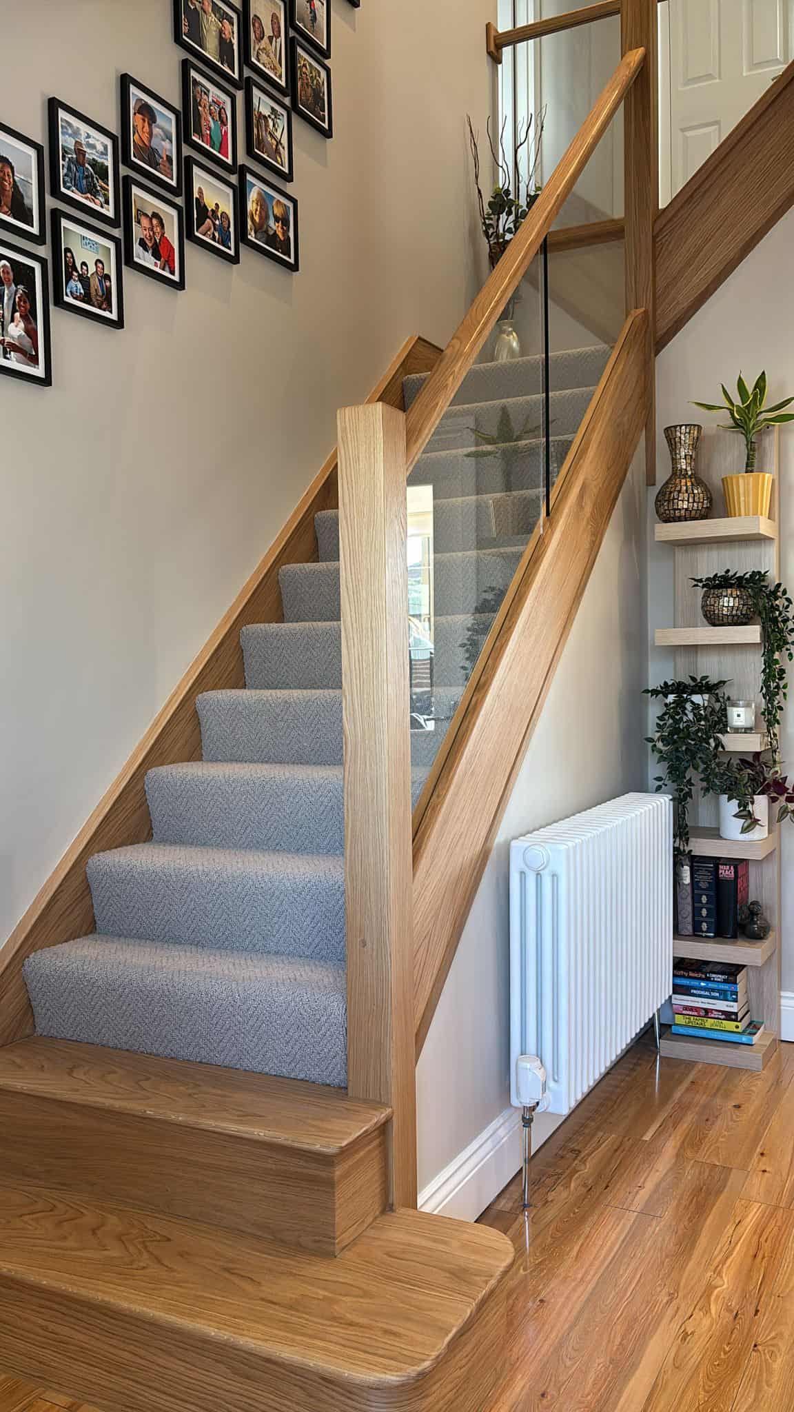Grey carpeted staircase with integrated oak and glass balustrades and two broad wooden feature steps beside a wall of framed photographs.