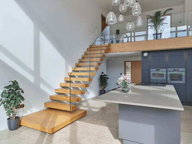 Floating oak staircase with frameless glass balustrades and a broad feature platform leading to a mezzanine above a contemporary kitchen.