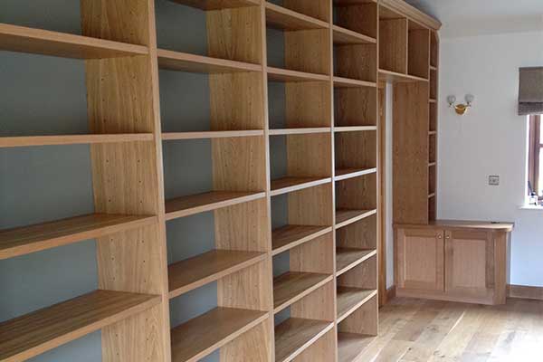 Wall-to-wall oak shelving with multiple open compartments and matching fitted base cupboards beside a window.