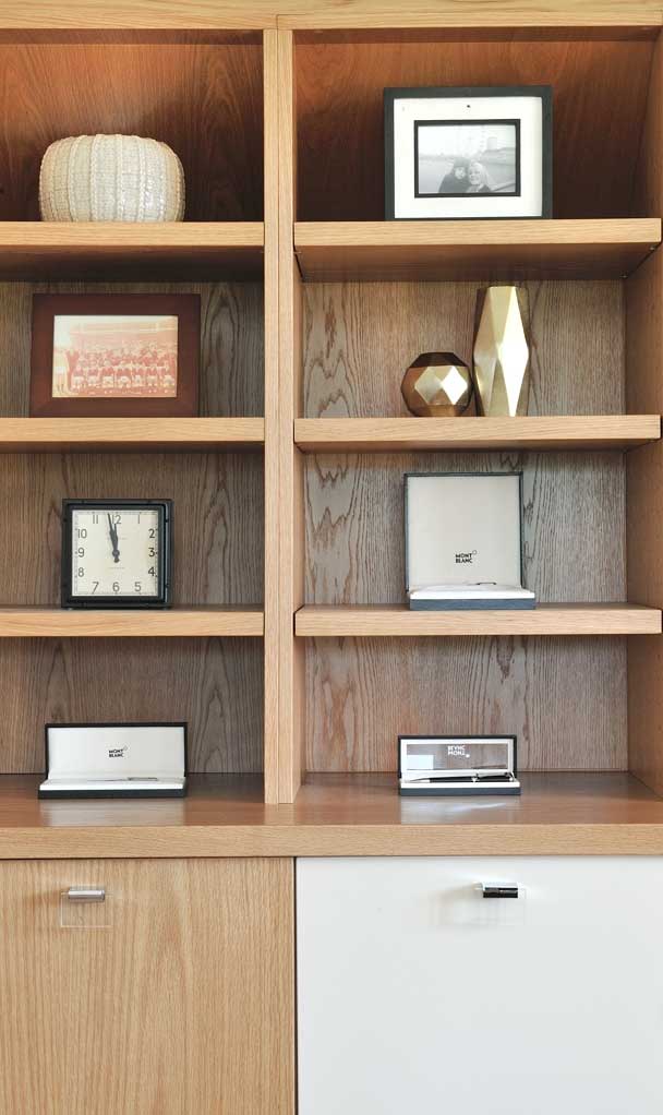 Fitted oak display shelves holding framed photographs, ornaments and a clock above contrasting oak and white cupboard doors.