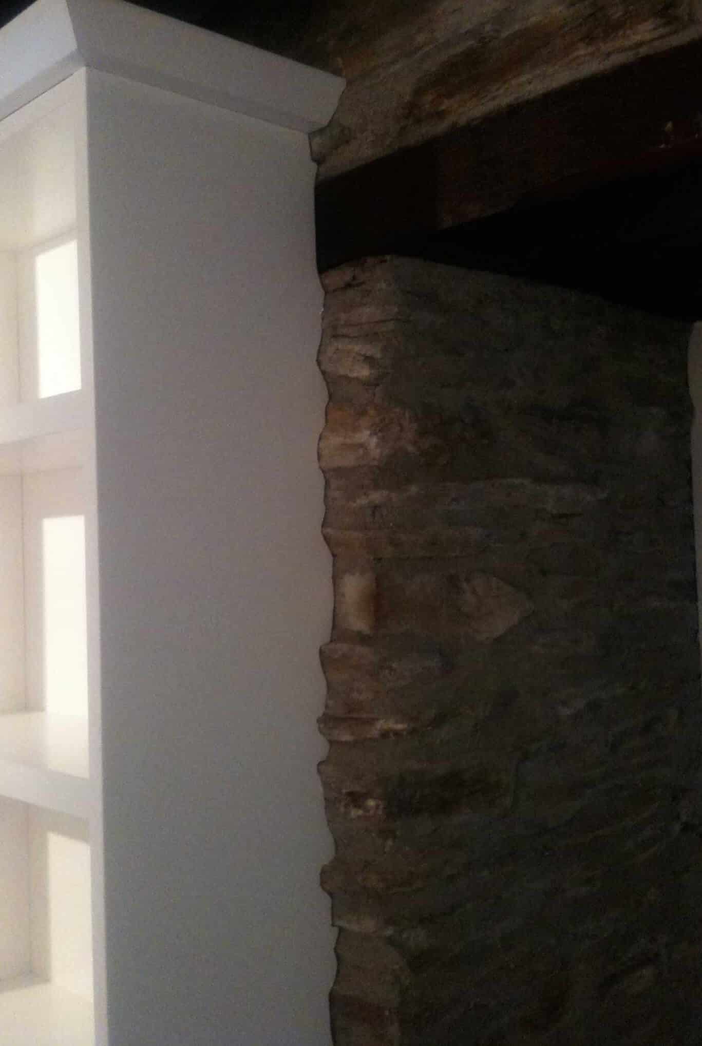 White fitted cabinet with inset frosted glass panels built beside an exposed stone wall beneath a dark timber beam.