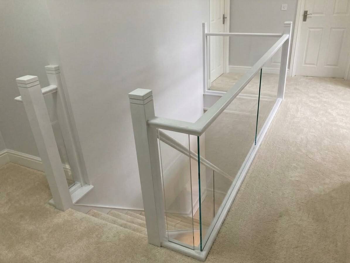 White-stained oak newel posts and rails framing clear glass panels around a cream carpeted landing and staircase.