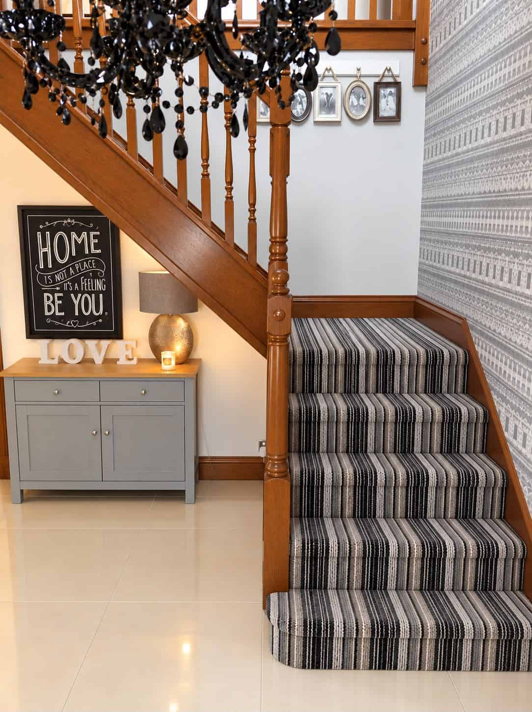Traditional wooden staircase with turned spindles, decorative newel posts and black, grey and white striped carpet.
