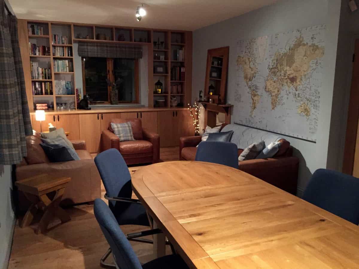 Home study with fitted oak bookshelves surrounding a window, matching base cupboards and a large wooden table beside leather seating.