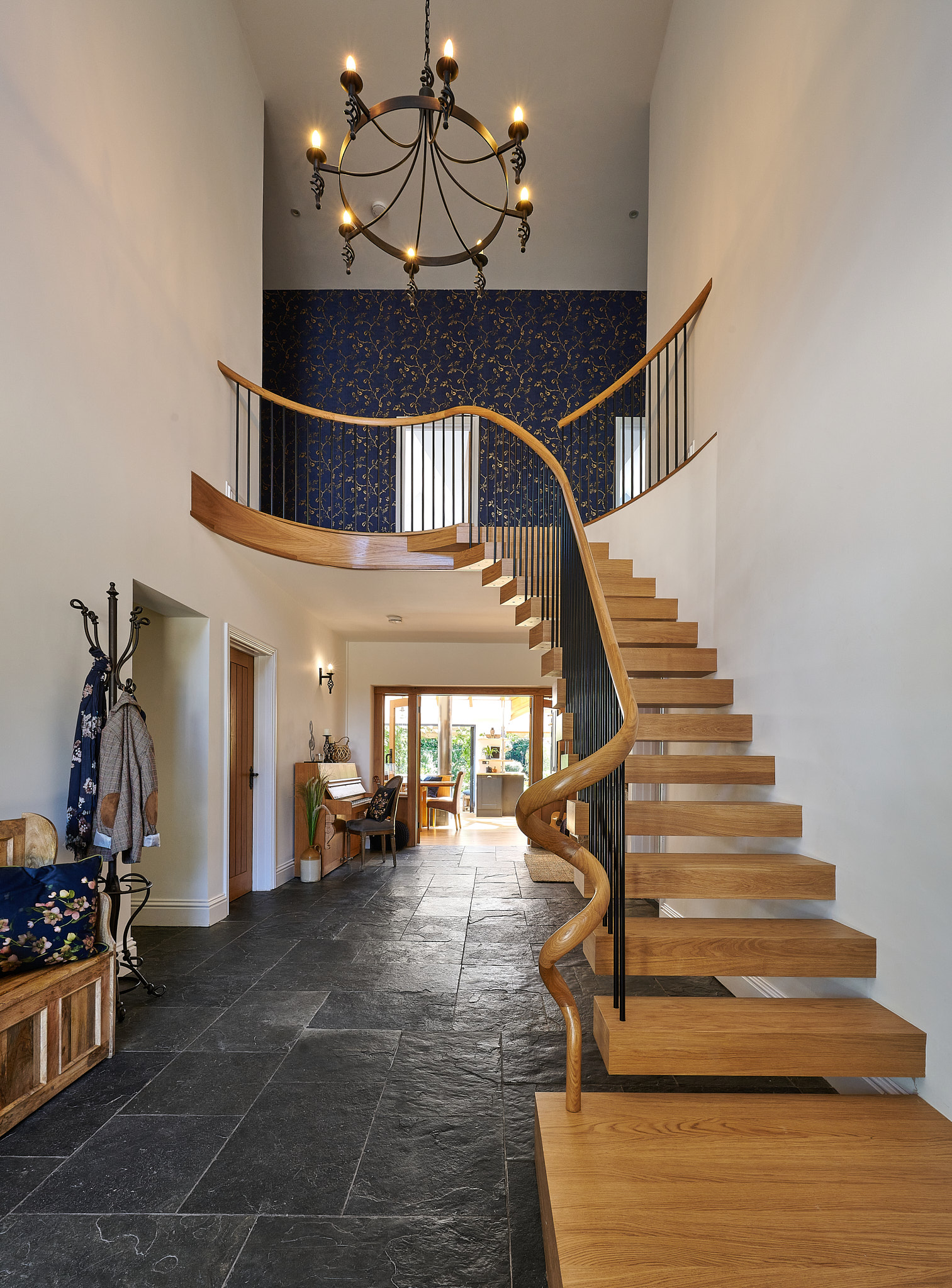Completed helical floating oak staircase with black spindles and a sweeping wooden handrail beneath a chandelier.