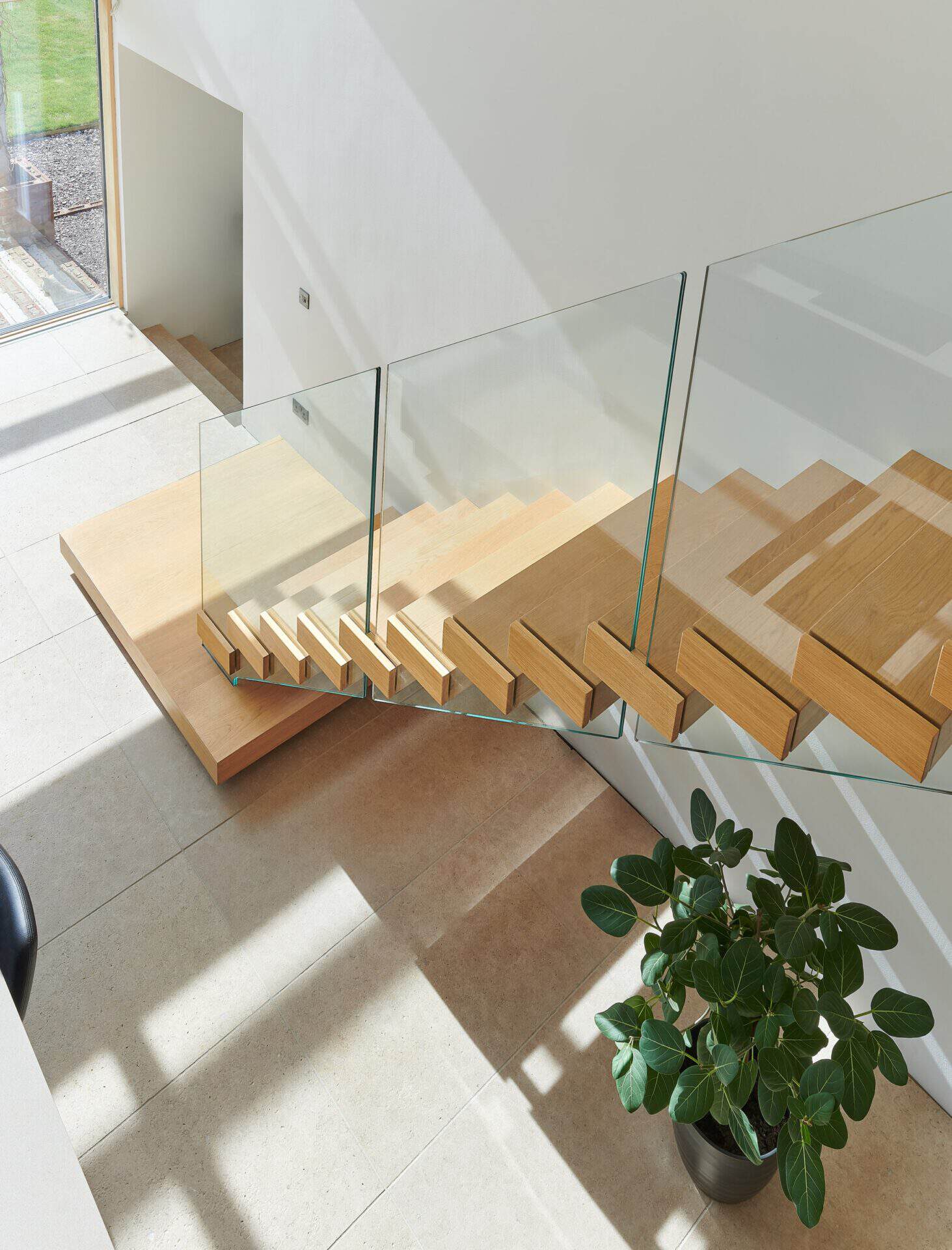View down an oak open-riser staircase with frameless glass balustrades and a broad wooden feature platform in the Nelms family home.