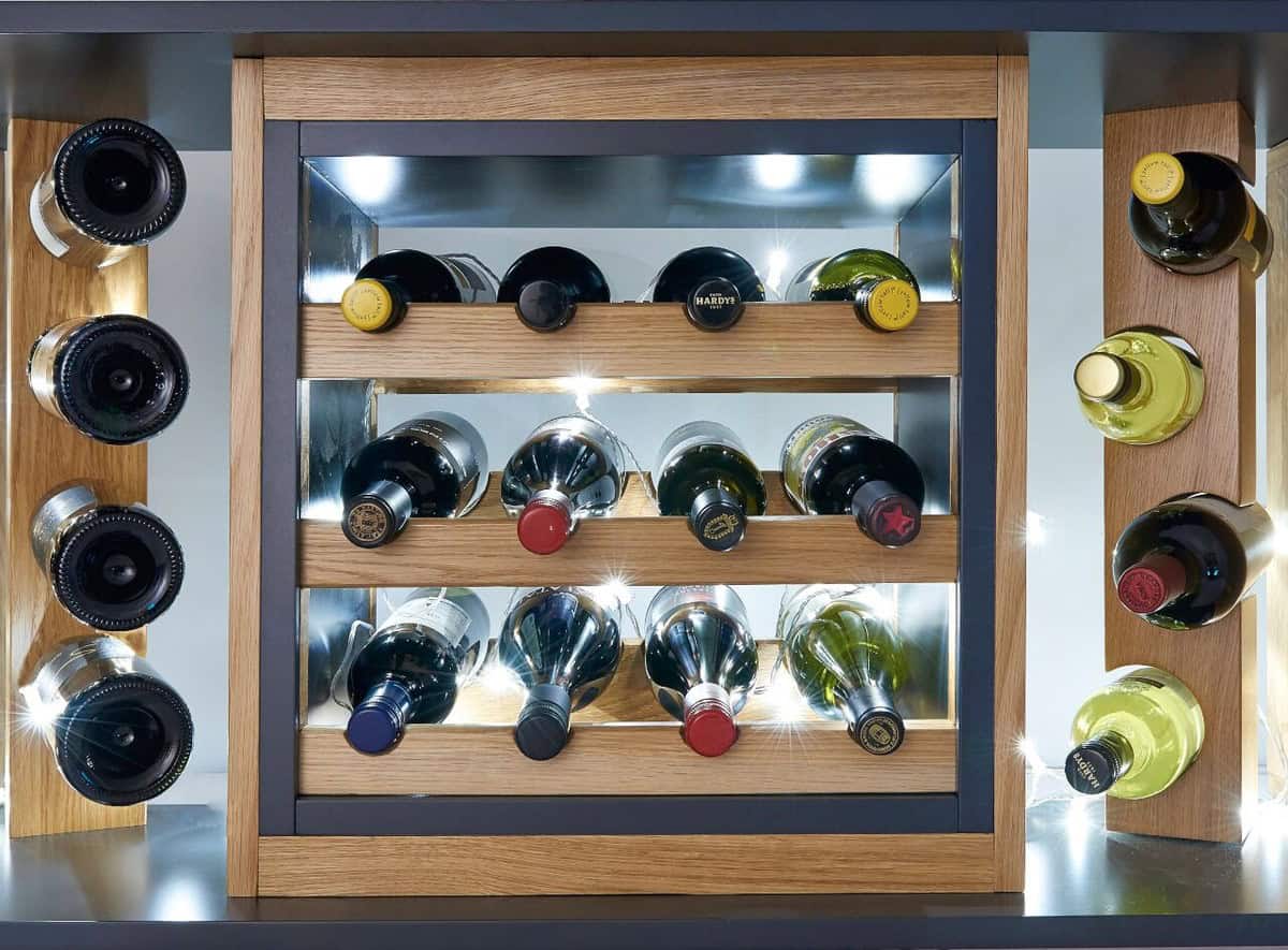 Close-up of illuminated oak wine storage with horizontal bottle racks, mirrored panels and vertical bottle displays on either side.
