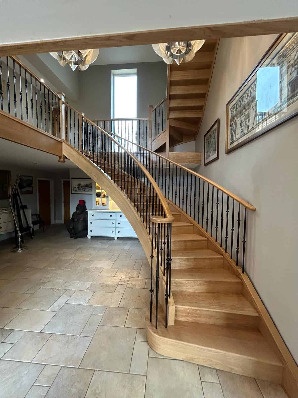Curved oak staircase with black metal spindles and a matching gallery landing in a double-height hallway.